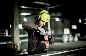 Mand der er ved at bore i metal. Han er udstyret med hjelm og arbejdstøj.