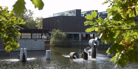 Albertslund Rådhus med rådhussøen og træer i forgrunden.